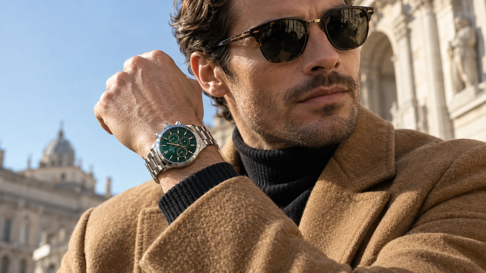 A man in a camel coat wearing a green-dial steel watch
